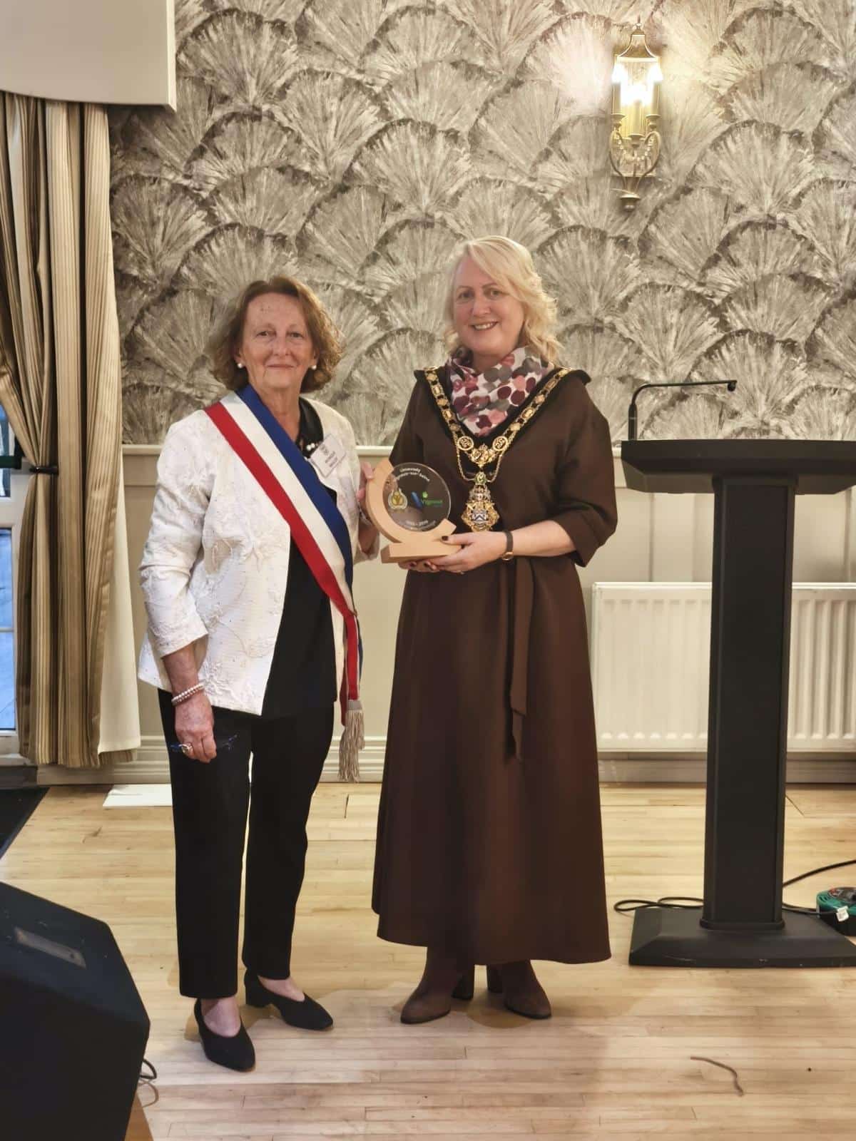 Monique Baillot, ceinte de l’écharpe tricolore, remet le trophée commémoratif des 30 ans du jumelage à Dawn Huggins